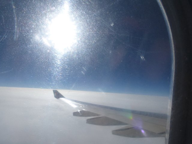 View of a plane wing from a passengers window with bright sun glare.