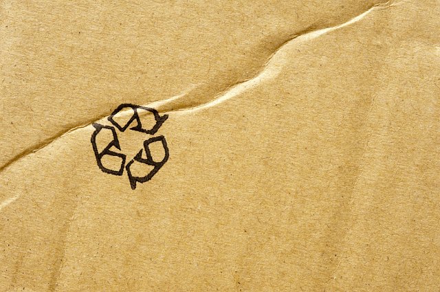 Recycle background of a black icon stamped in the corner of brown cardboard packaging with copy space viewed from above