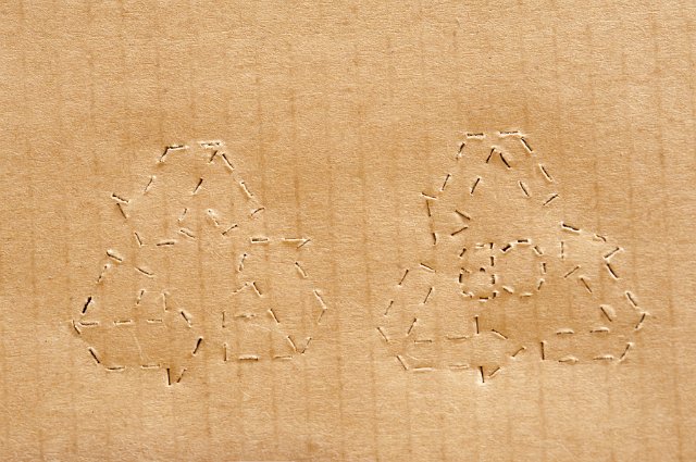 Close up view on pair of perforated recycle symbols in brown corrugated cardboard sheet