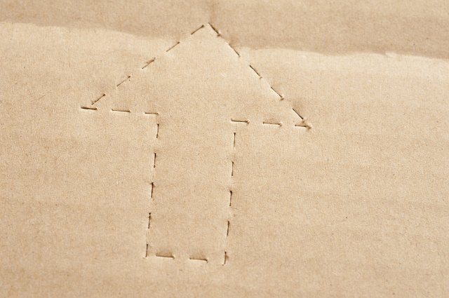 This way up perforated arrow stamped into a brown cardboard packing carton or box, close up view