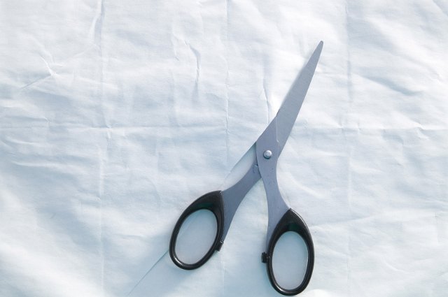 background in cold light with a pair of scissors half cut across a sheet of wrinkled paper