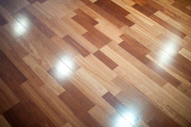 Polished shiny floor made from short laminated planks reflecting the light from four overhead spots