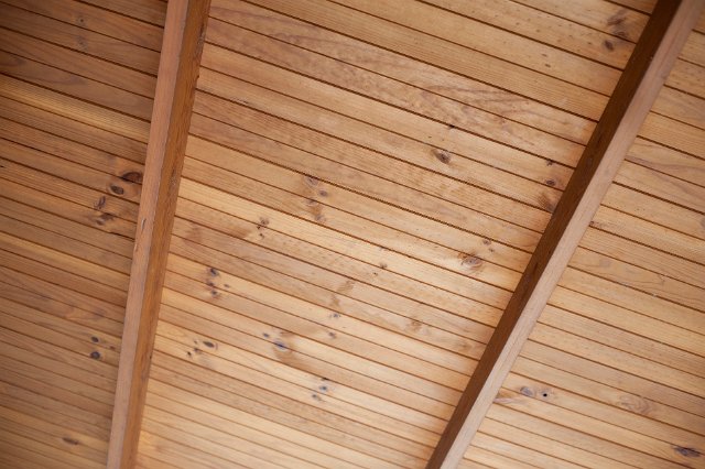 View from underneath of a wooden ceiling made from natural unpolished wooden planks on cross beams