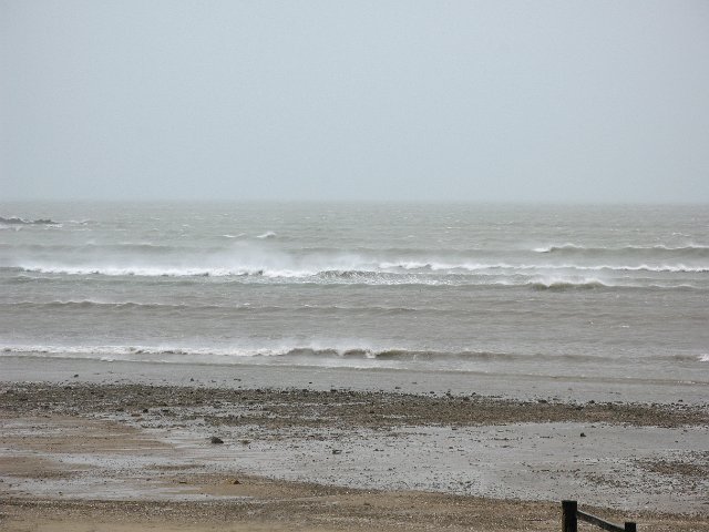 grey oceanscape with a strong wind blowing spray of waves